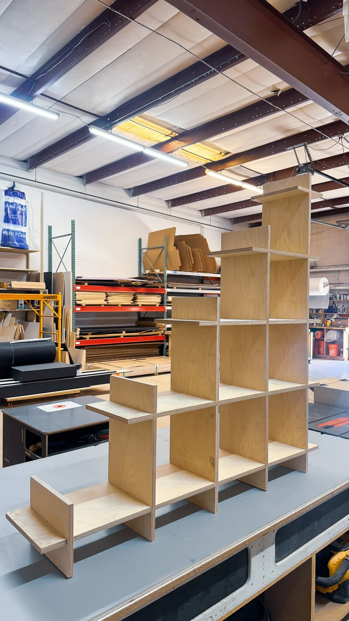 Wooden shelving unit in a workshop, with assorted tools and materials in the background.