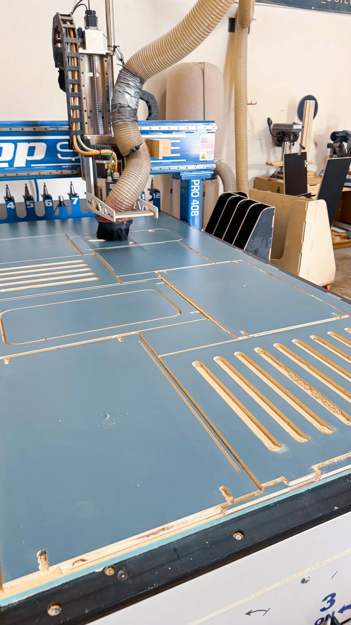 Close-up of a CNC machine or laser cutter with a metal sheet secured on the bed, some wood pieces and a large duct hose connected to the machine for ventilation.