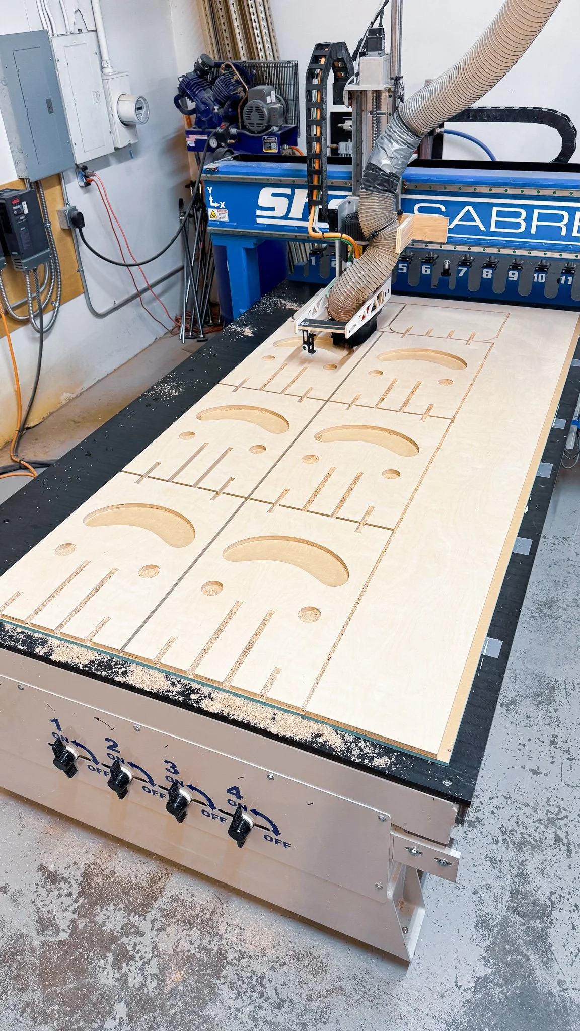 A CNC woodworking machine cutting holes and shapes into a large sheet of plywood.
