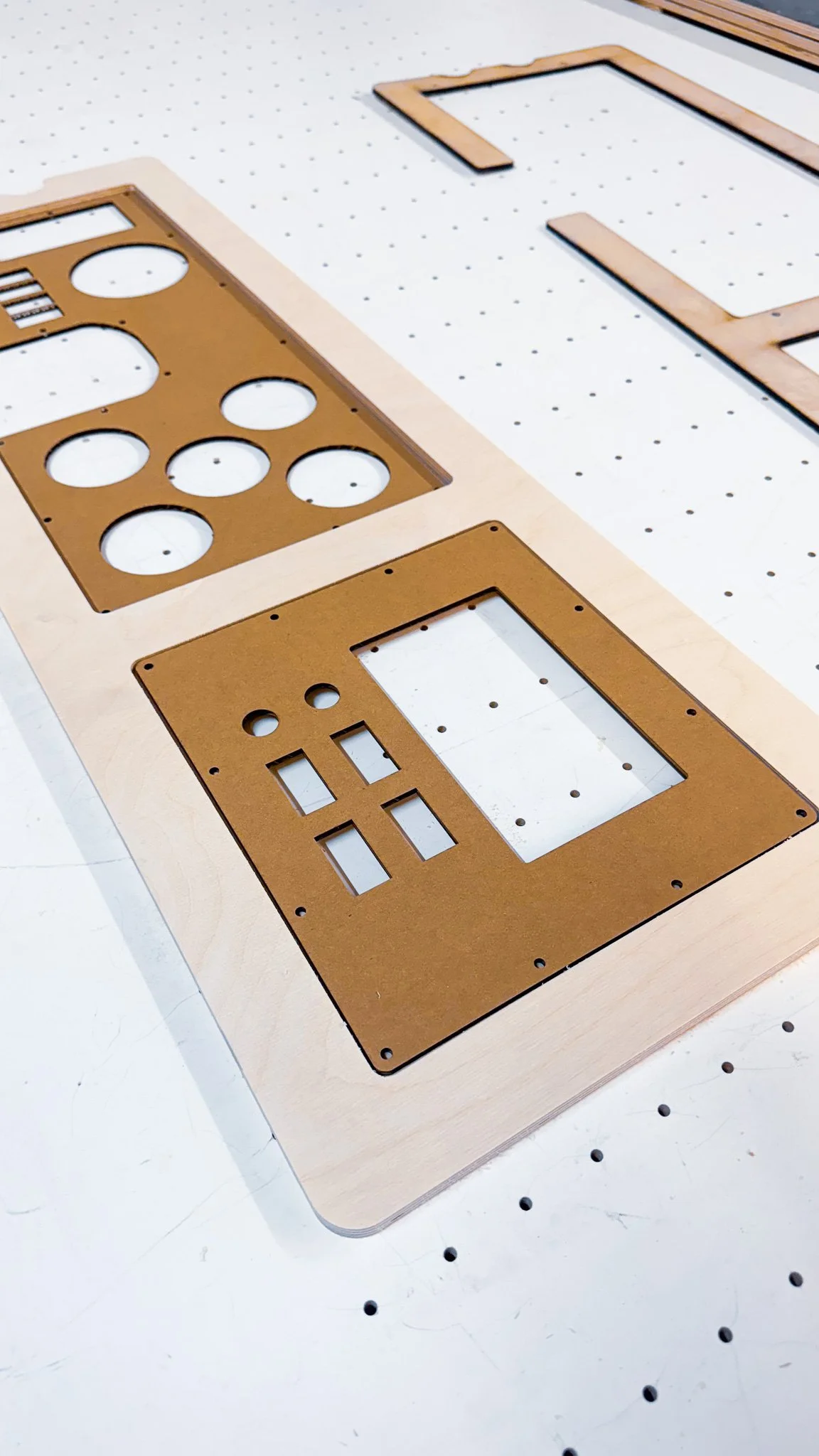 Wooden circuit board with cutouts for electronic components, placed on a white pegboard with holes.