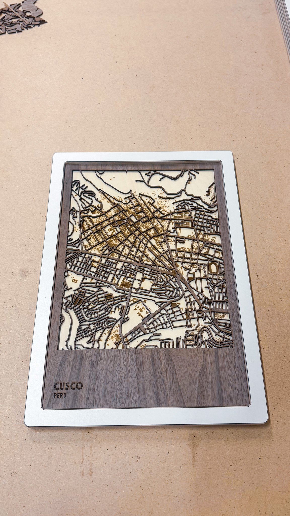 A detailed wooden map of Cusco, Peru, with streets and terrain features, set in a decorative frame.