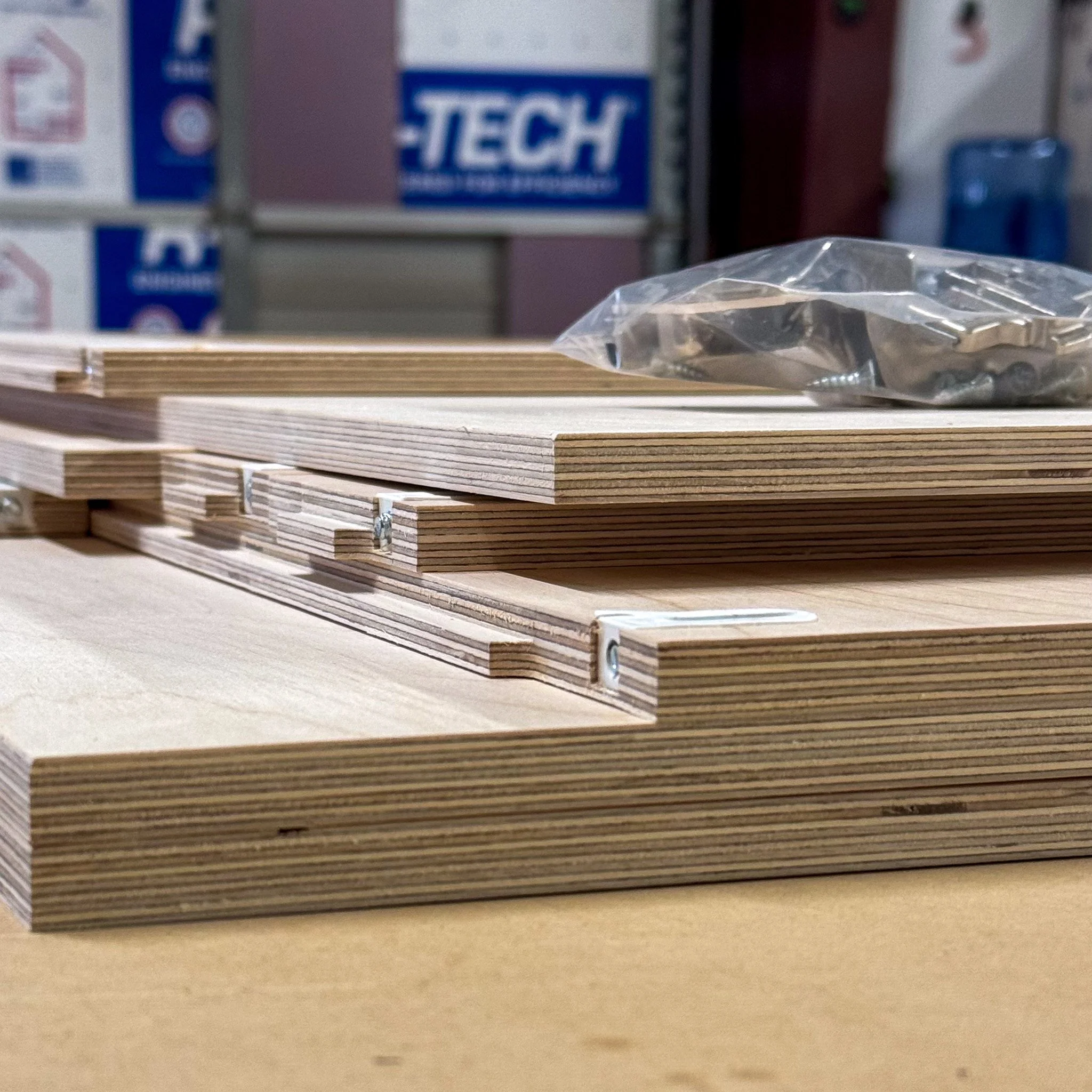 Close-up of stacked plywood sheets and hardware on a workbench in a hardware store.