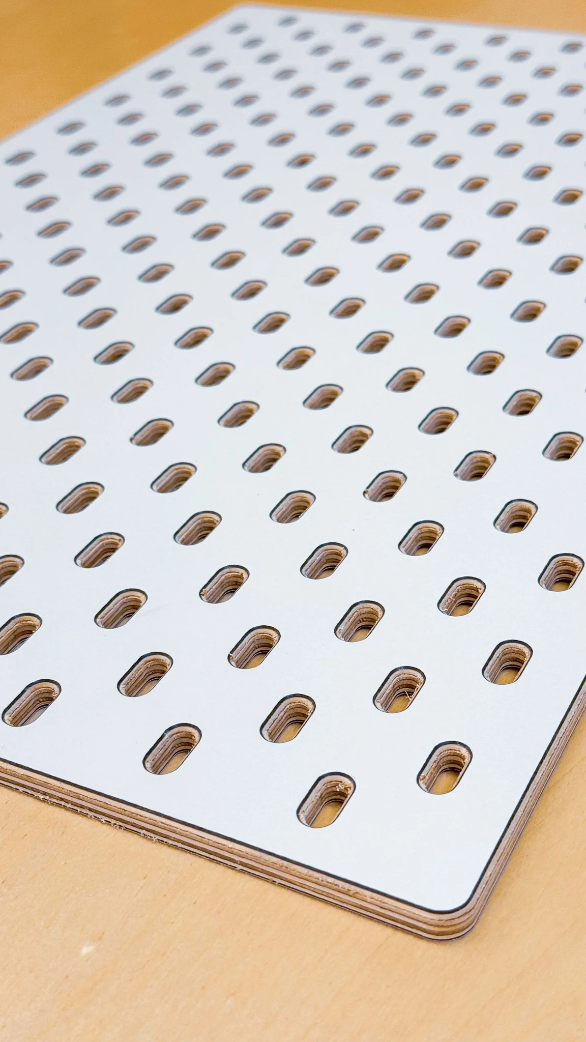 A white laminated sheet of paper with numerous small oval holes on a light-colored table.