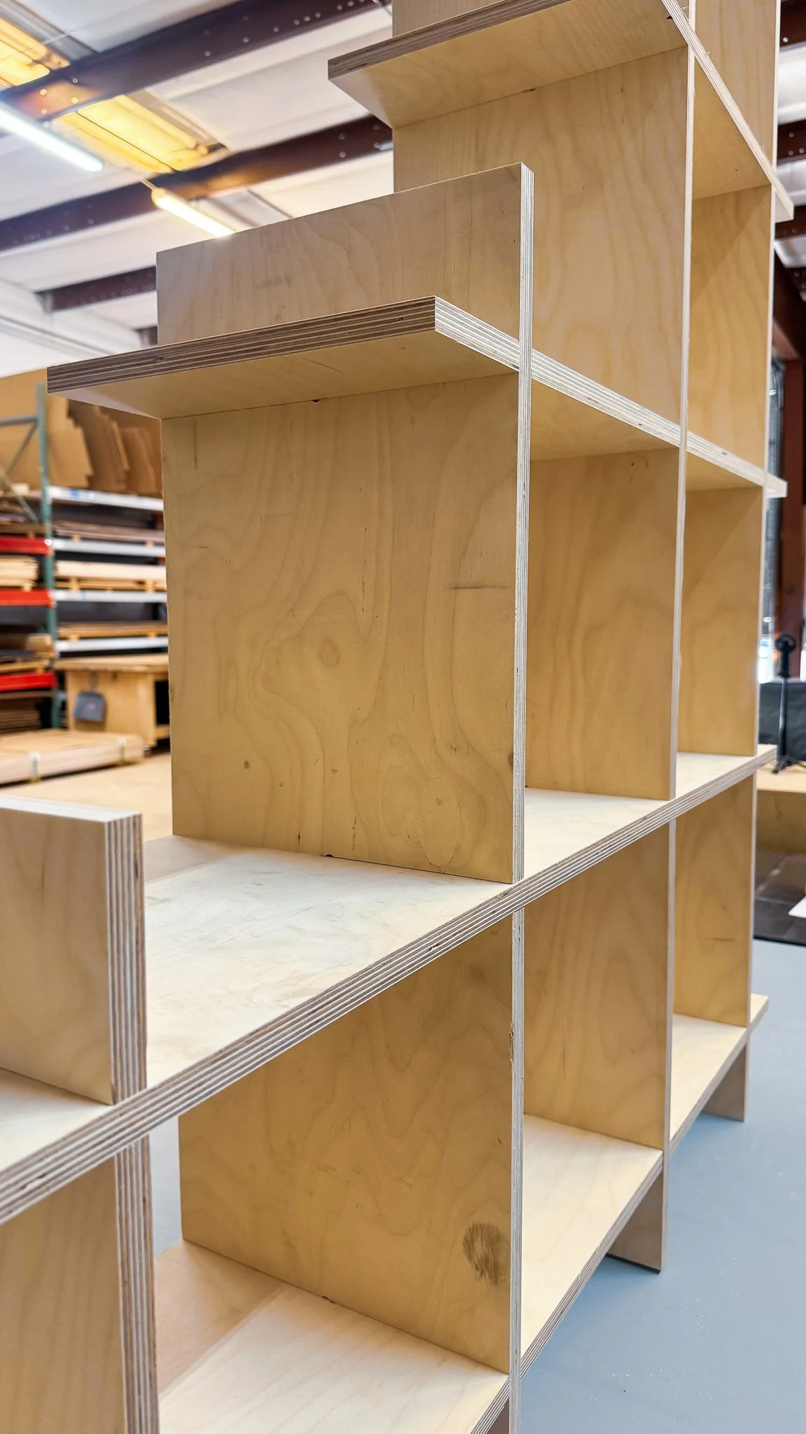 Wooden shelving unit with multiple sections, shown in a workshop or warehouse setting.
