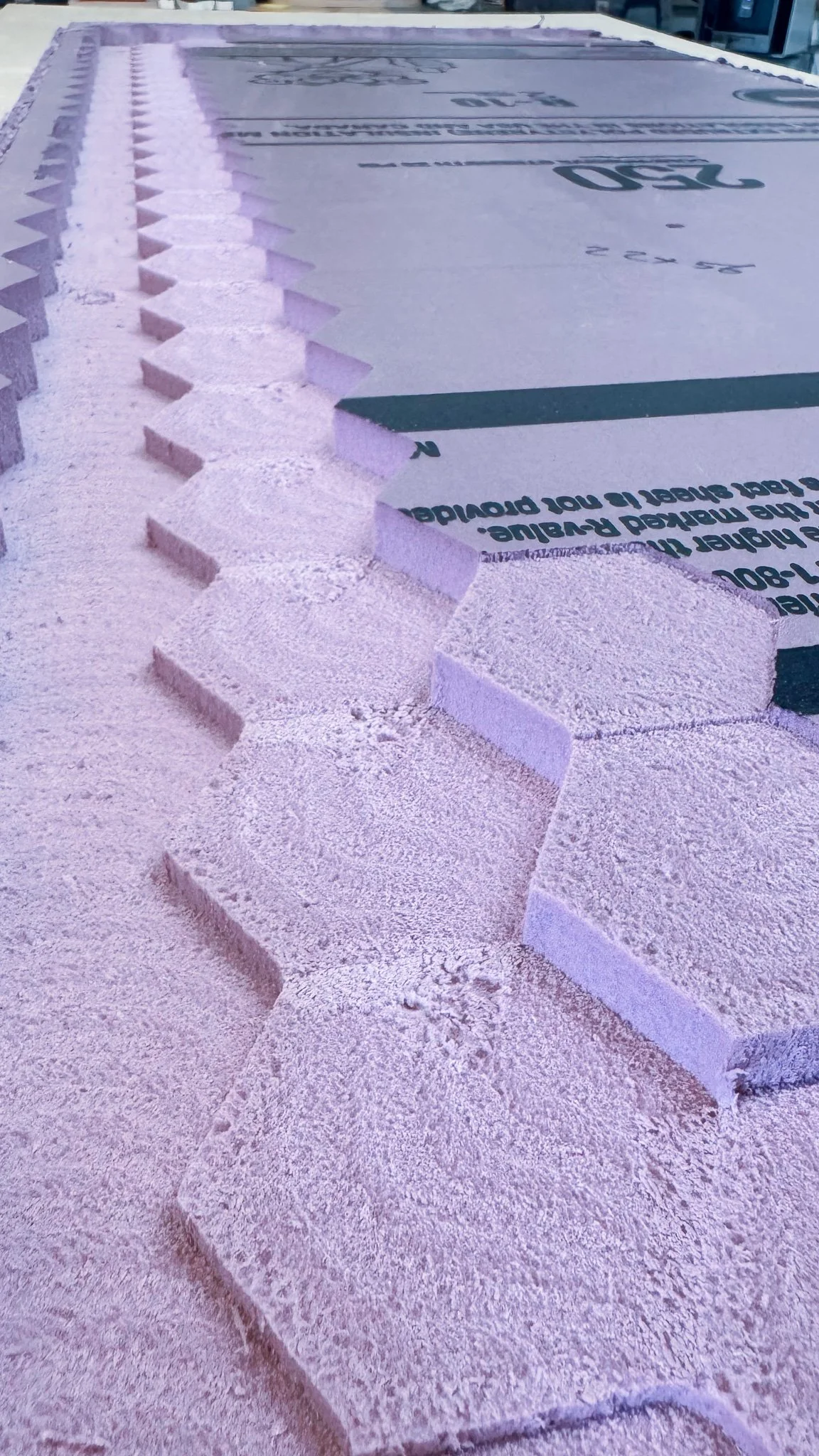 Close-up view of a sheet of pink foam insulation that has been carved with a CNC router machine.