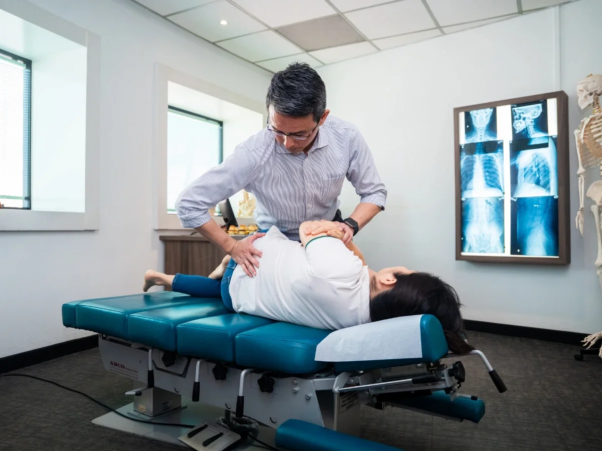 Chiropractor performing spinal adjustment on patient lying on treatment table