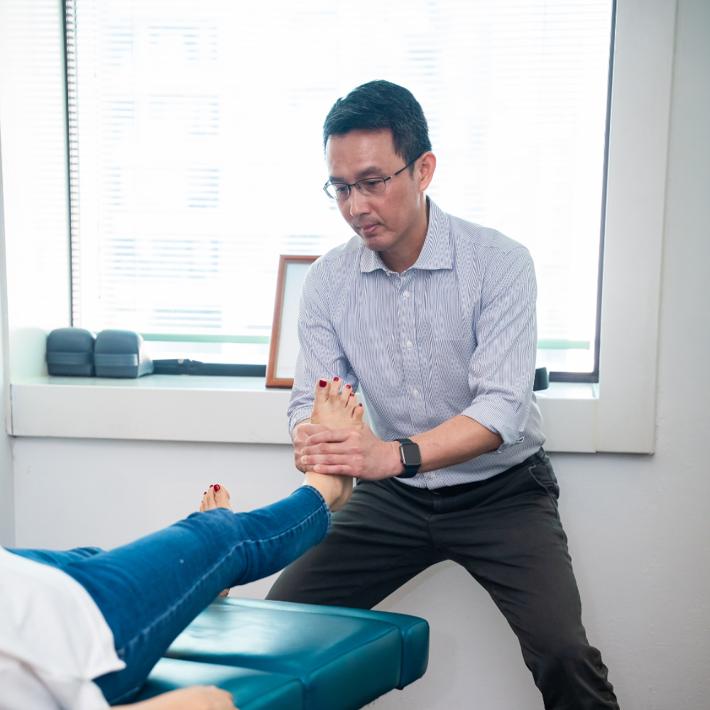 Chiropractor performing manual adjustment on patient’s leg in clinic