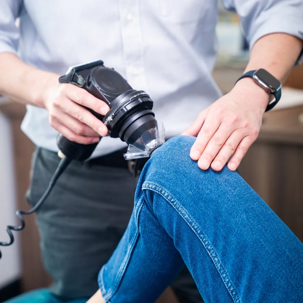 Chiropractor using therapy device on patient’s knee during treatment