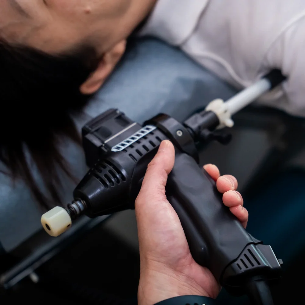 Chiropractor using therapy device on patient’s shoulder during treatment