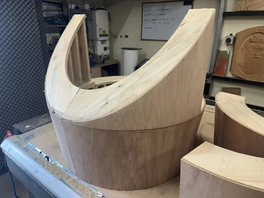 Wooden curved structure in a woodworking shop, possibly a piece of furniture or a sculpture in progress.