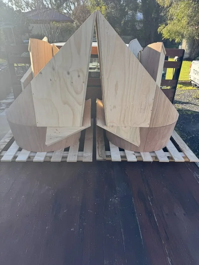 Unfinished wooden boat sitting on a pallet outdoors.