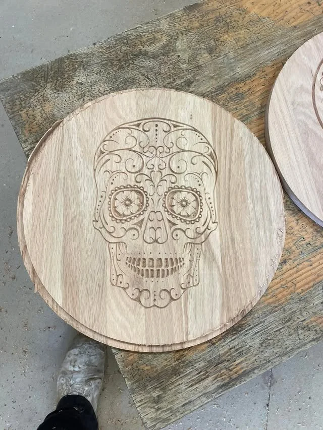 Round wooden board with a detailed skull design carved into it, resting on a wooden workbench.