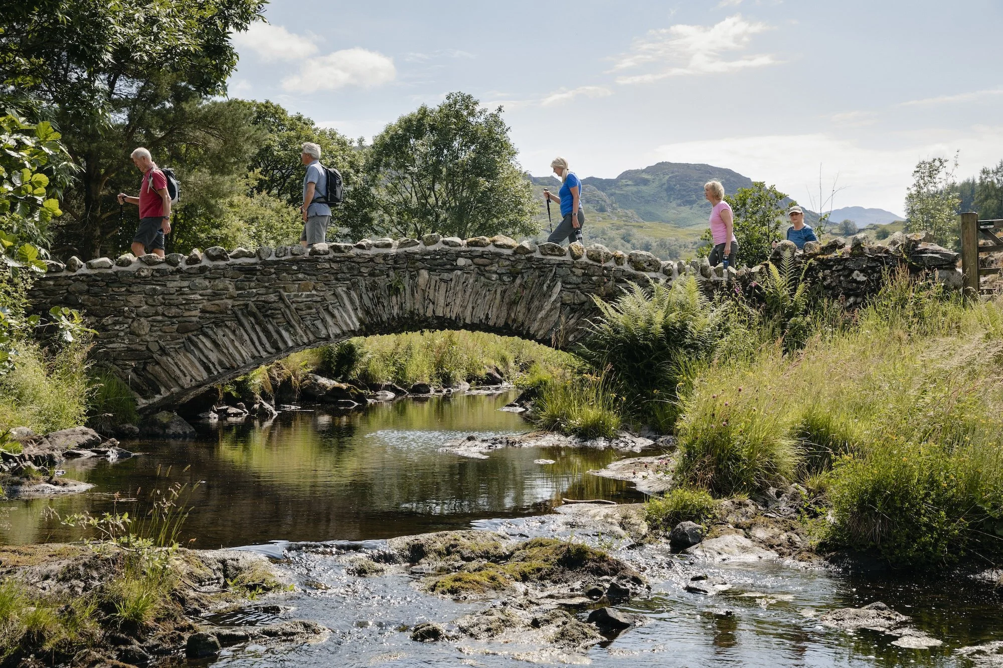 An older group of hikers cross a bridge in the British countryside