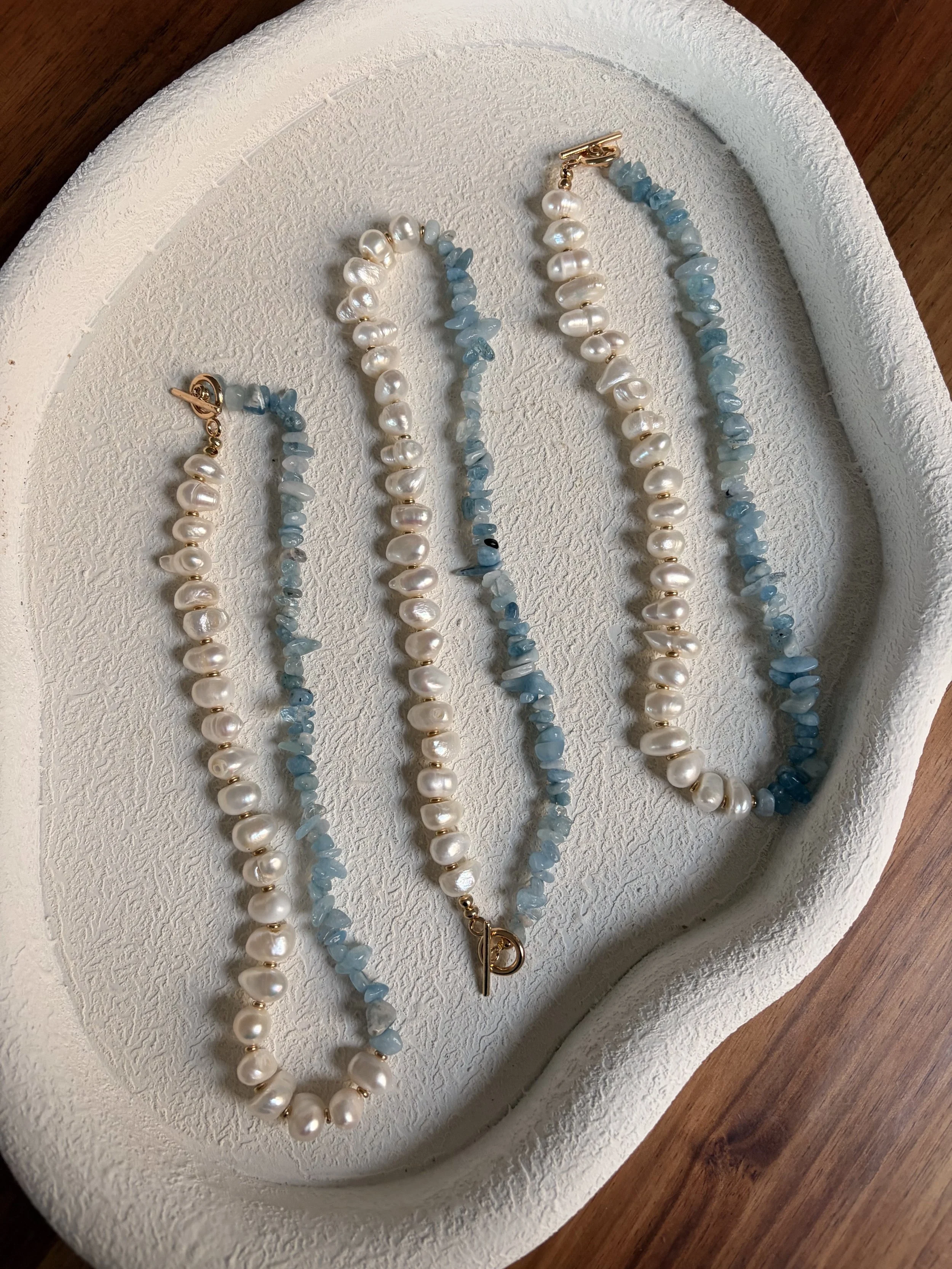 A jewelry display tray with two pearl necklaces and two blue stone necklaces, arranged in parallel.