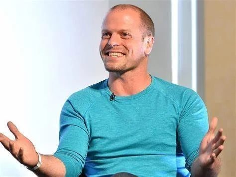 A smiling man in a teal long-sleeve shirt gesturing with his hands during a discussion or interview.