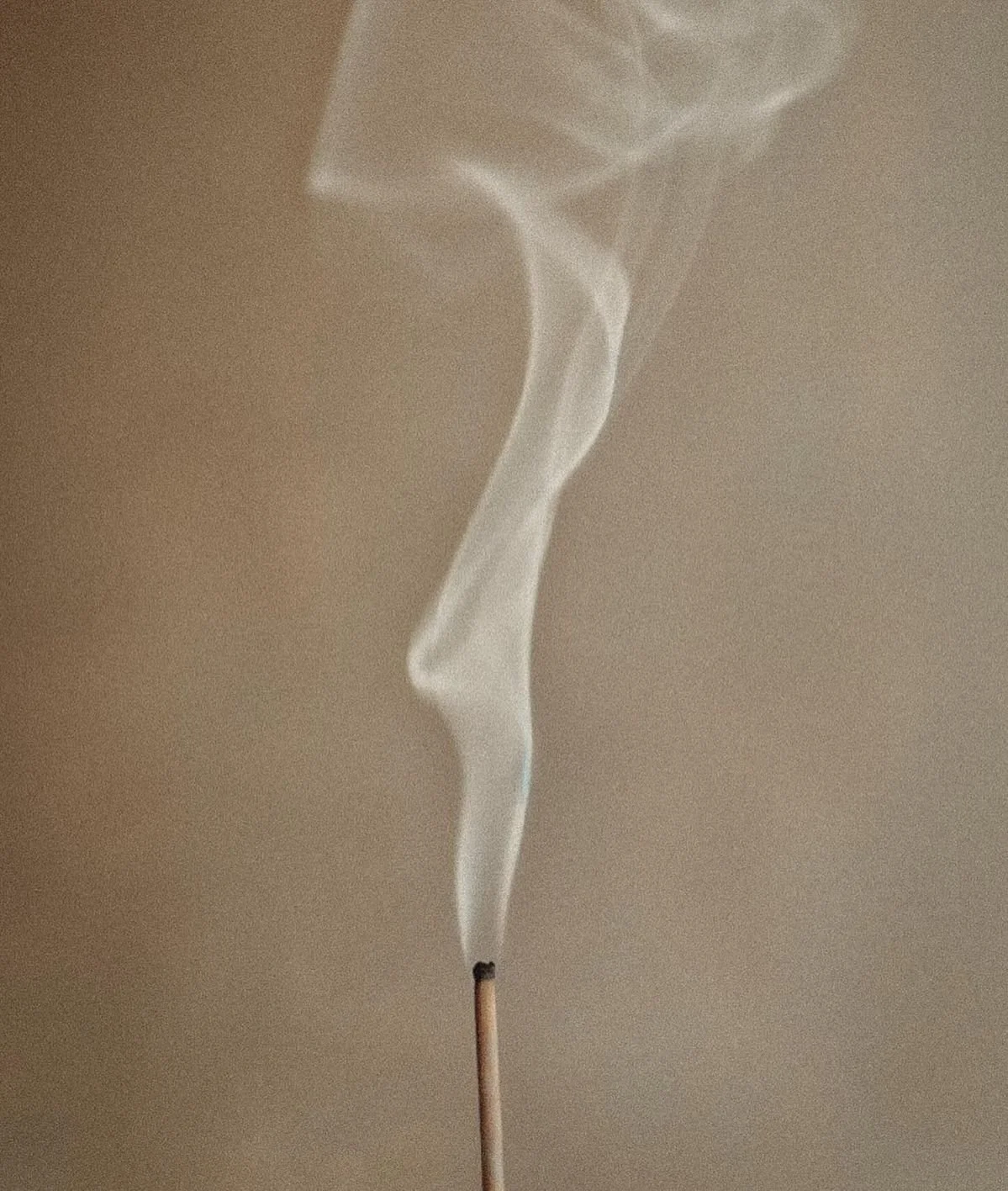 Une allumette allumée avec de la fumée qui s'élève en spirale contre un fond neutre.