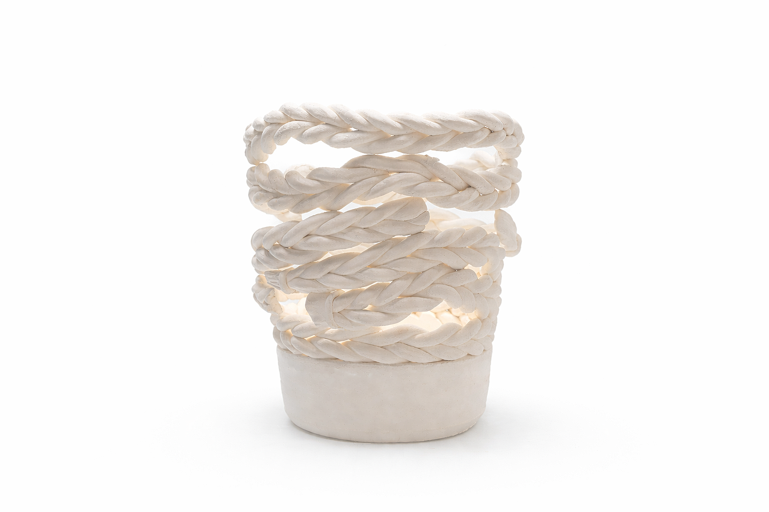 A white ceramic candle holder with five woven braided rings stacked on top of each other, illuminated from within against a white background.