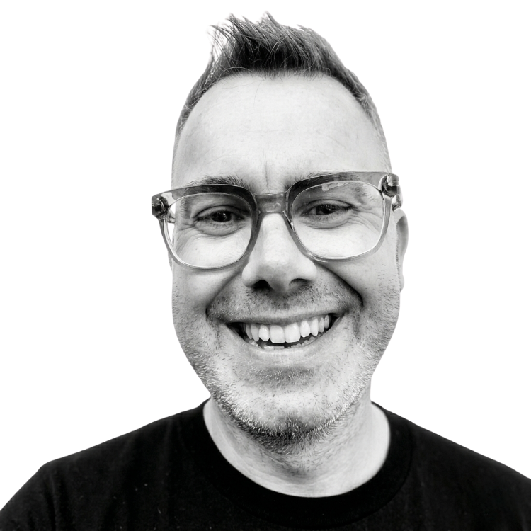 A smiling man with glasses and short hair, wearing a black shirt, in a black and white photo.