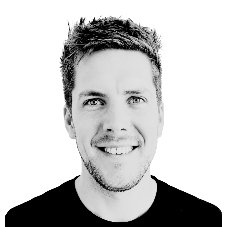 Black and white portrait of a smiling young man with short hair and light facial hair, wearing a dark shirt, against a black background.