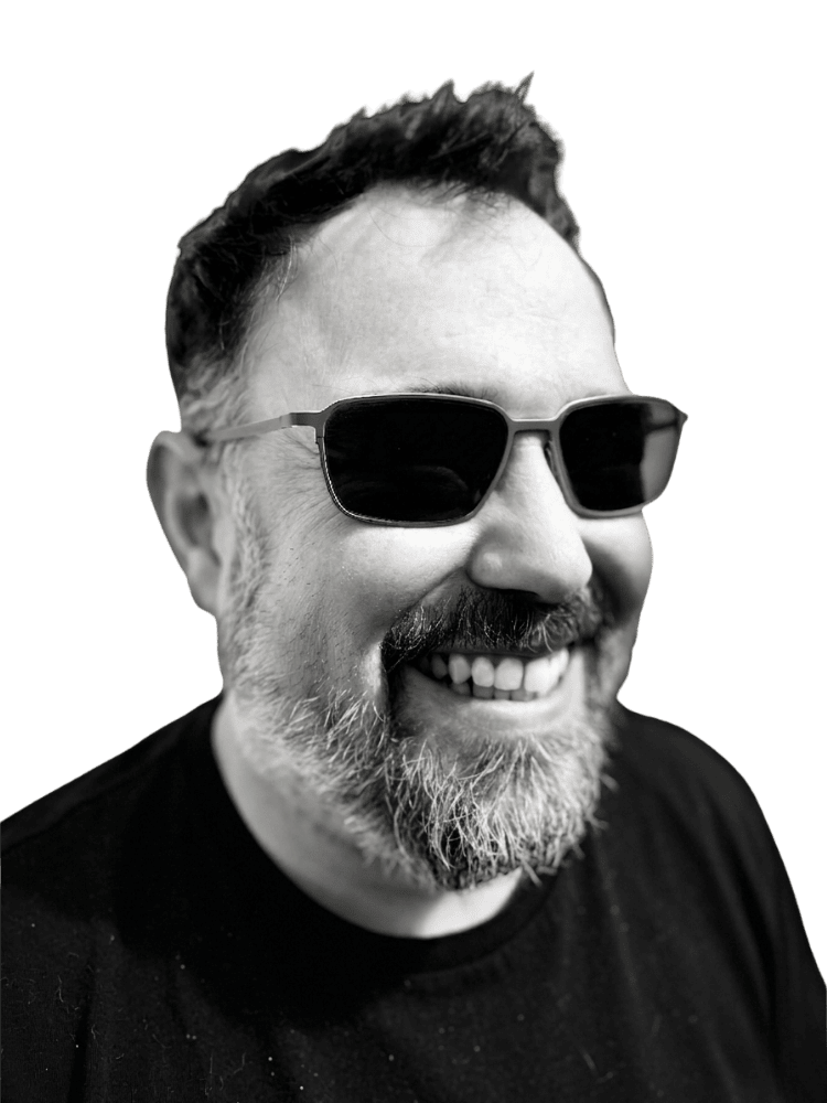 Black and white photo of a smiling man with a beard wearing sunglasses and a black shirt.