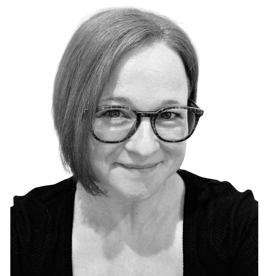 Black-and-white close-up of a woman with short hair, wearing glasses, smiling, and wearing a dark top.