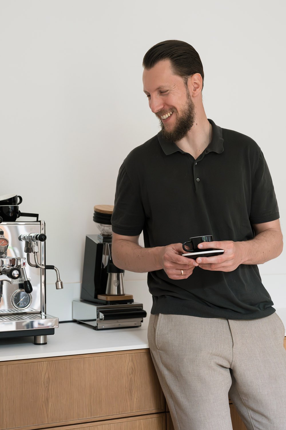 Coffee Coach founder holding an espresso cup beside a home espresso machine during a home barista coaching session.