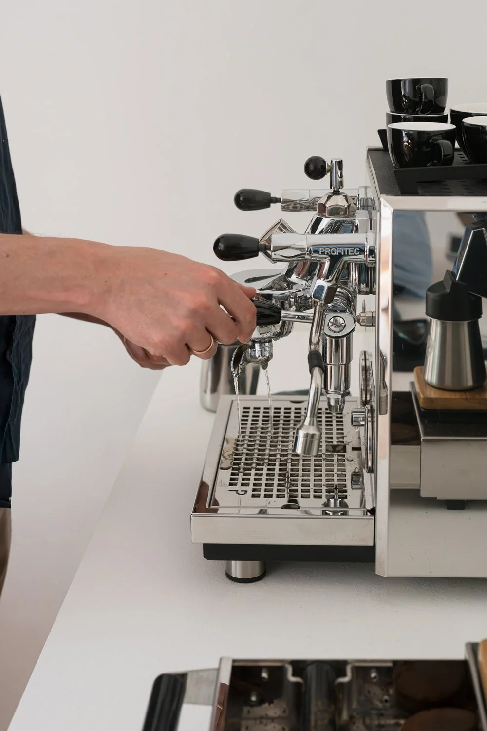 Home-Barista bereitet Espresso an einer Profitec Siebträgermaschine zu, mit gestapelten ACME Tassen bereit zum Servieren.