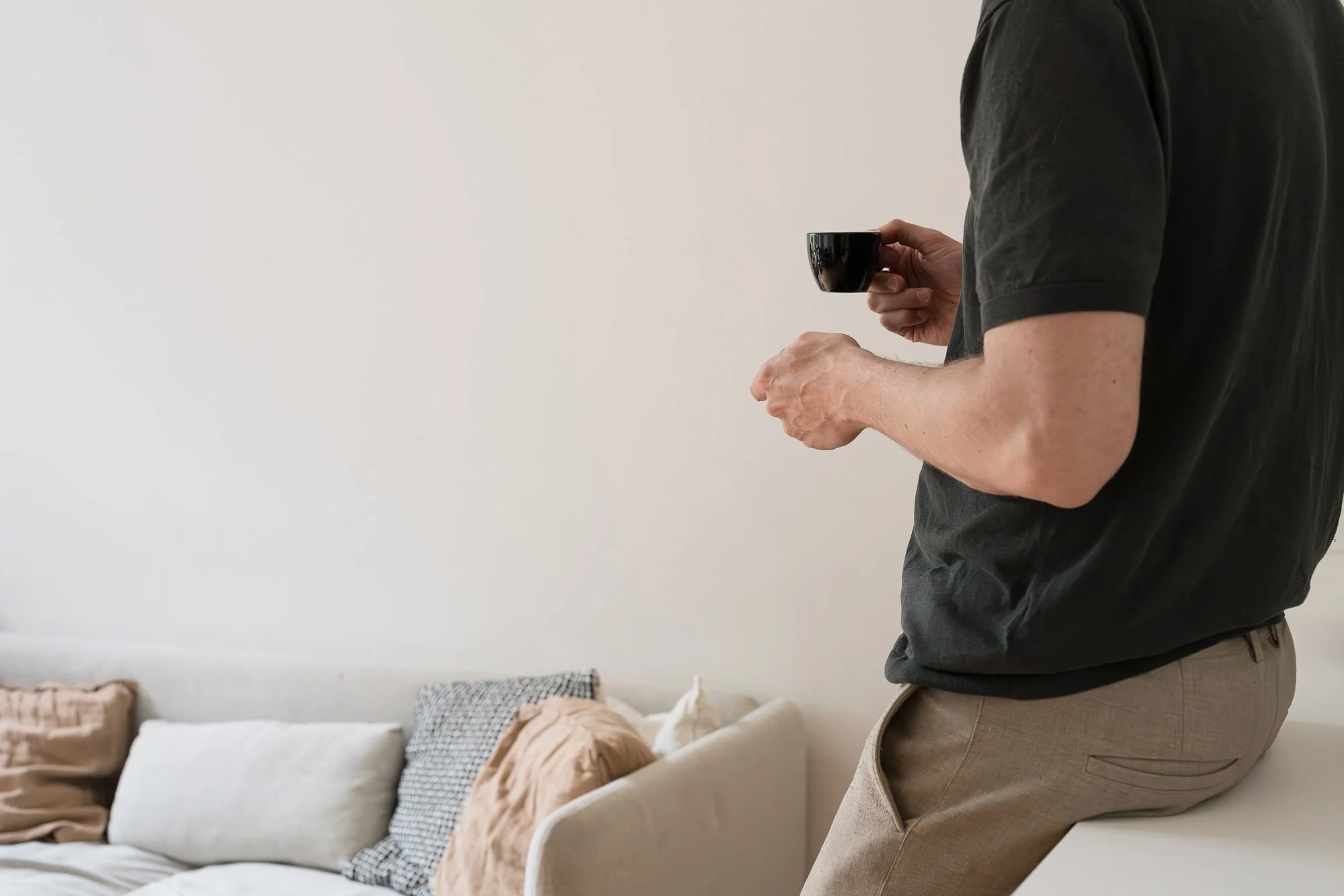 Home-Barista hält eine Tasse Espresso in einem modernen Wohnzimmer nach der Zubereitung von hochwertigem Kaffee zu Hause.