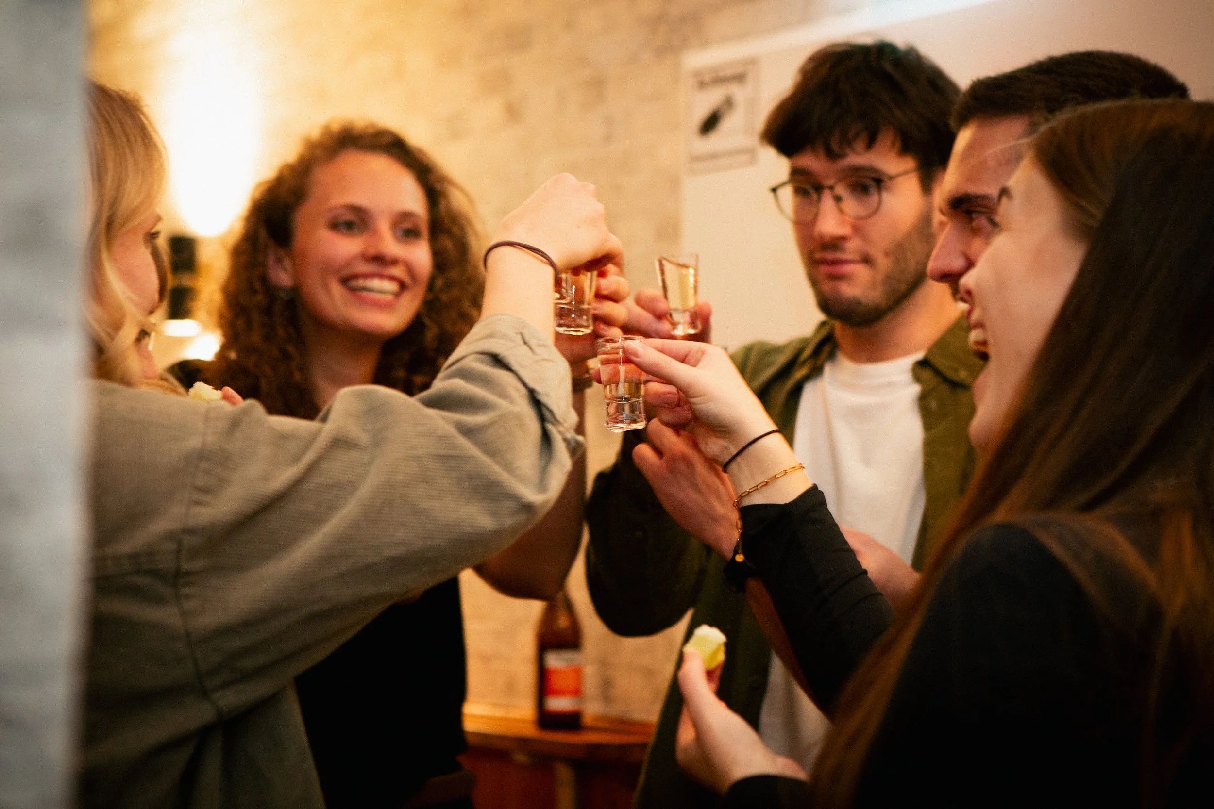 Group of five young adults enjoying drinks and food together at a social gathering or party.