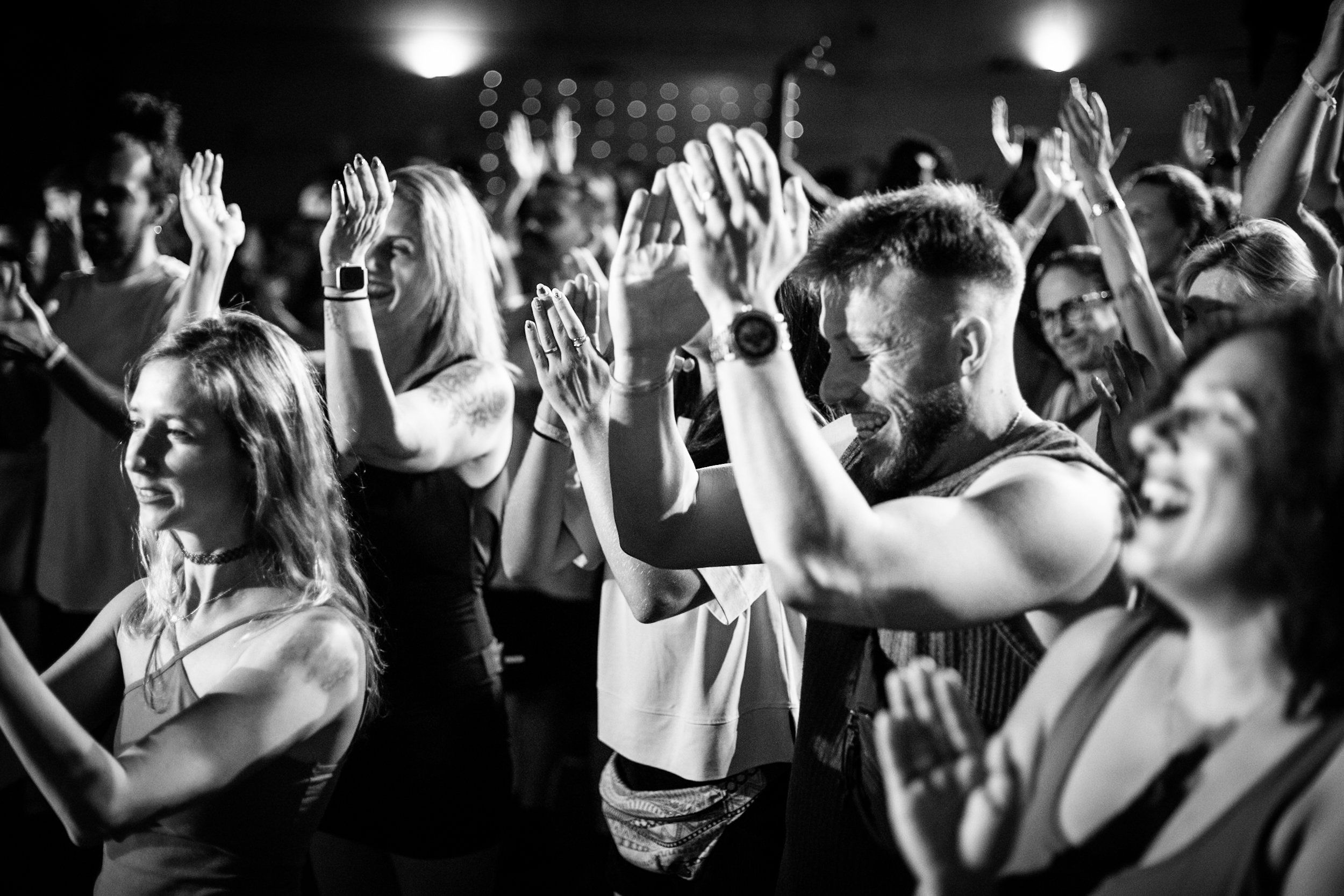Black and white photo of a group of people at a concert or event, with hands raised and smiling faces, enjoying the moment.