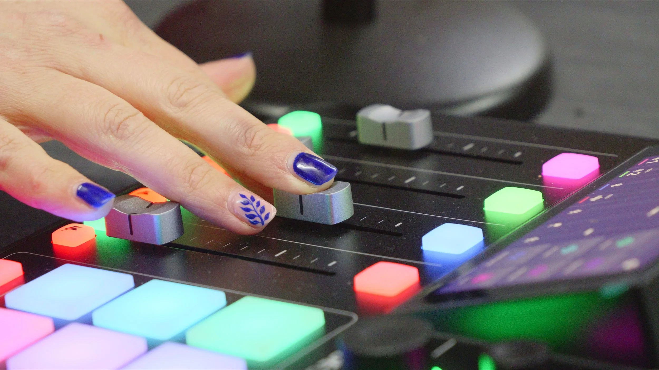 A person's hand with decorated nails adjusting input levels on a Rodecaster with colorful backlit buttons and sliders.