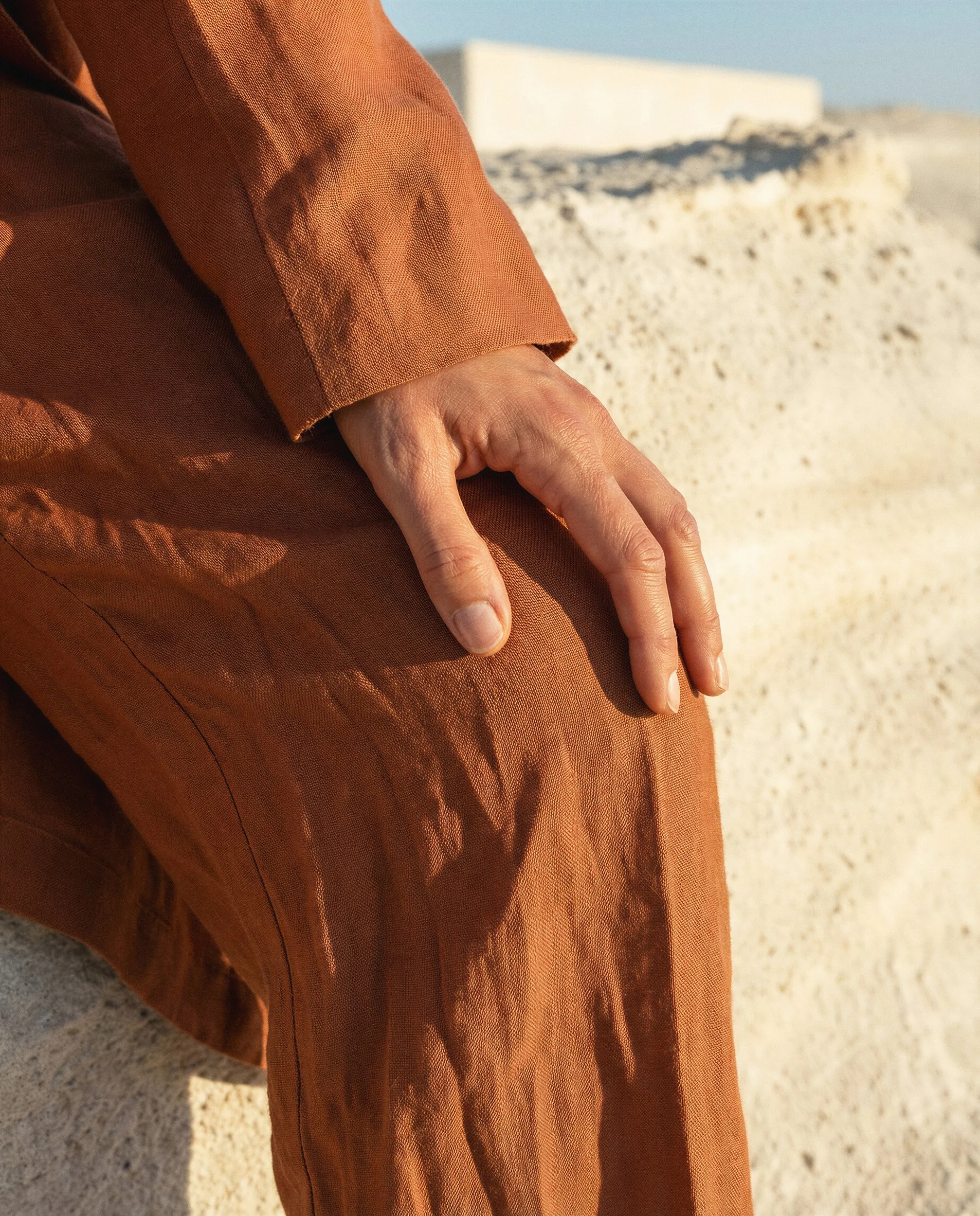 "Extreme macro shot of a hand resting on orange linen trousers, focusing on the fabric weave and realistic skin detail. This visual highlights the hyper-realistic material fidelity achieved by The Raw Lab's AI engine."