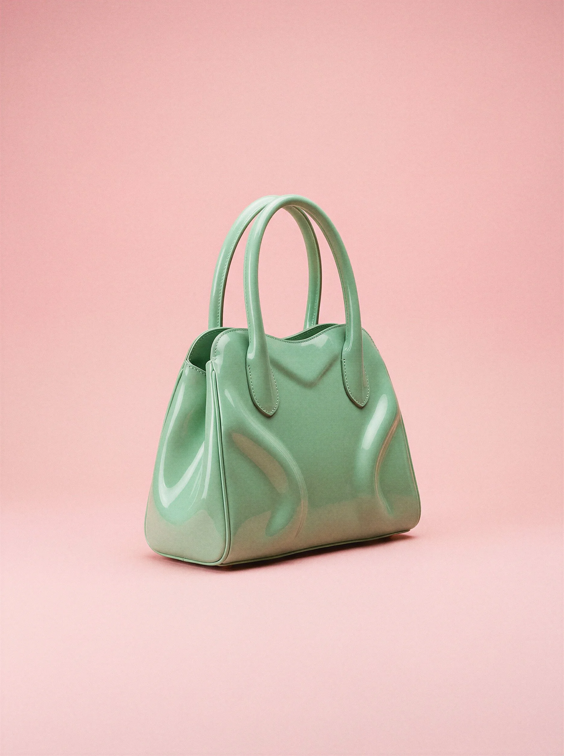 "Professional studio product photography of a mint green glossy handbag on a soft pink background. Demonstrating the clean aesthetics and light accuracy of synthetic commercial imagery for luxury brands."