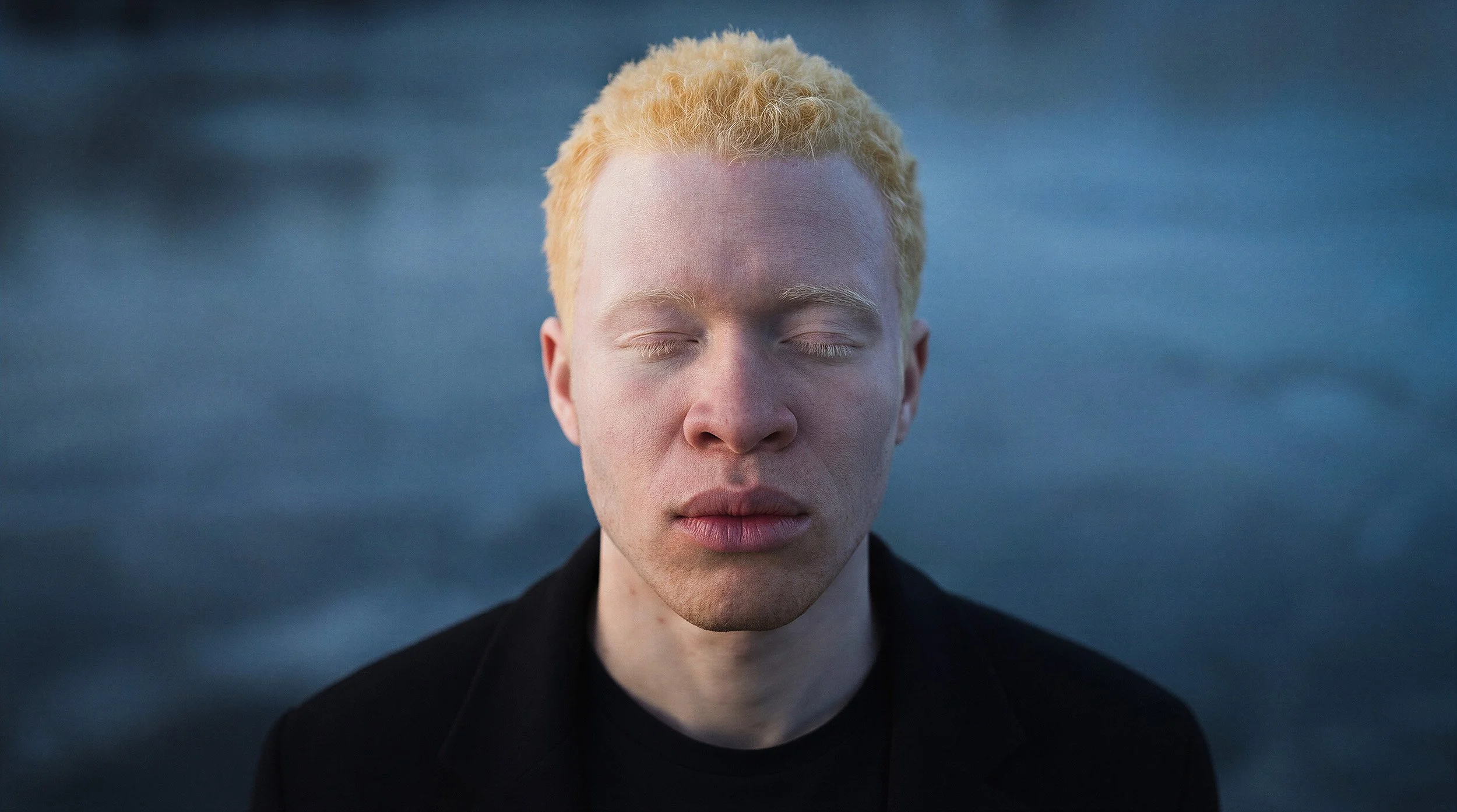 "Detailed portrait of a male model with eyes closed against a blurred arctic background. Showcasing the emotional depth and skin texture realism of digital twin technology."