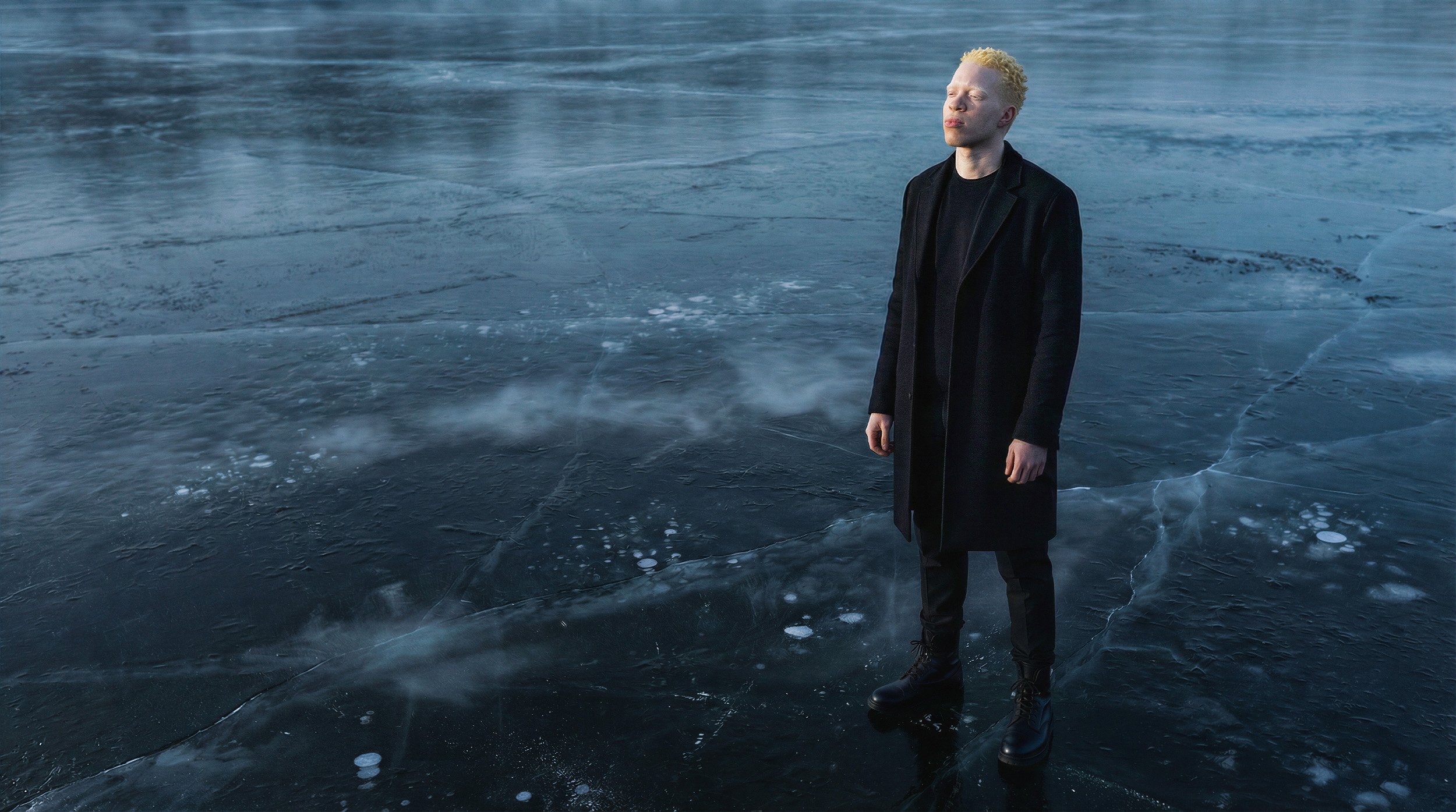 "Full body shot of a digital twin male model wearing a structured black wool coat on a misty, cracked ice field. Synthetic fashion photography for The Arctic Void campaign."