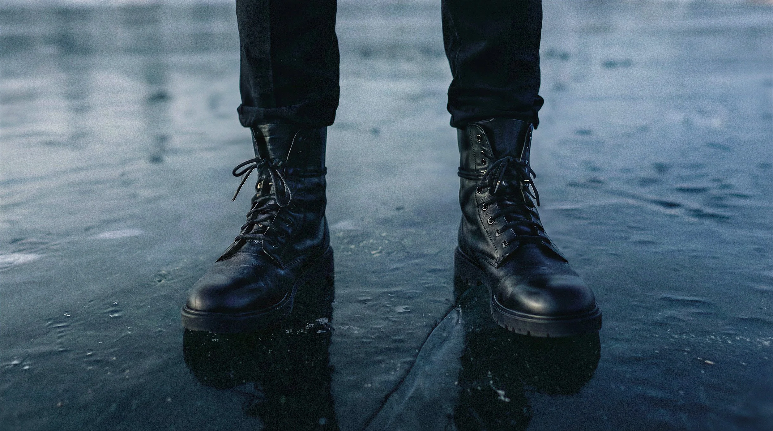 "Close-up of structured black leather boots standing on a cracked glacial surface. High-fashion footwear detail from The Raw Lab Arctic Void campaign, demonstrating hyper-realistic AI textures."