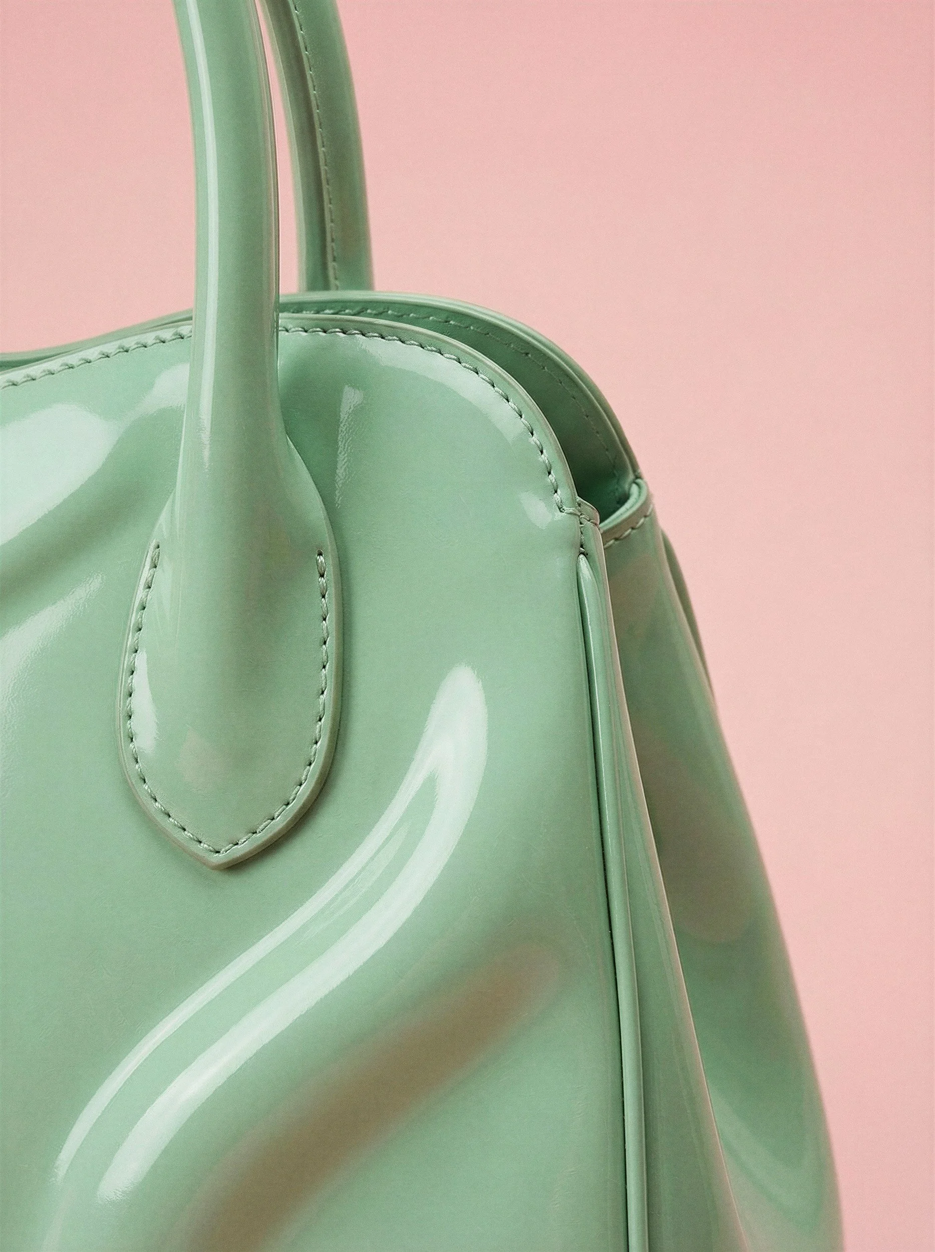 "Close-up detail of a glossy mint green leather handbag against a pink background. This visual highlights hyper-realistic material textures, precision stitching, and light reflections achieved through The Raw Lab's AI visual engine in Lisbon."