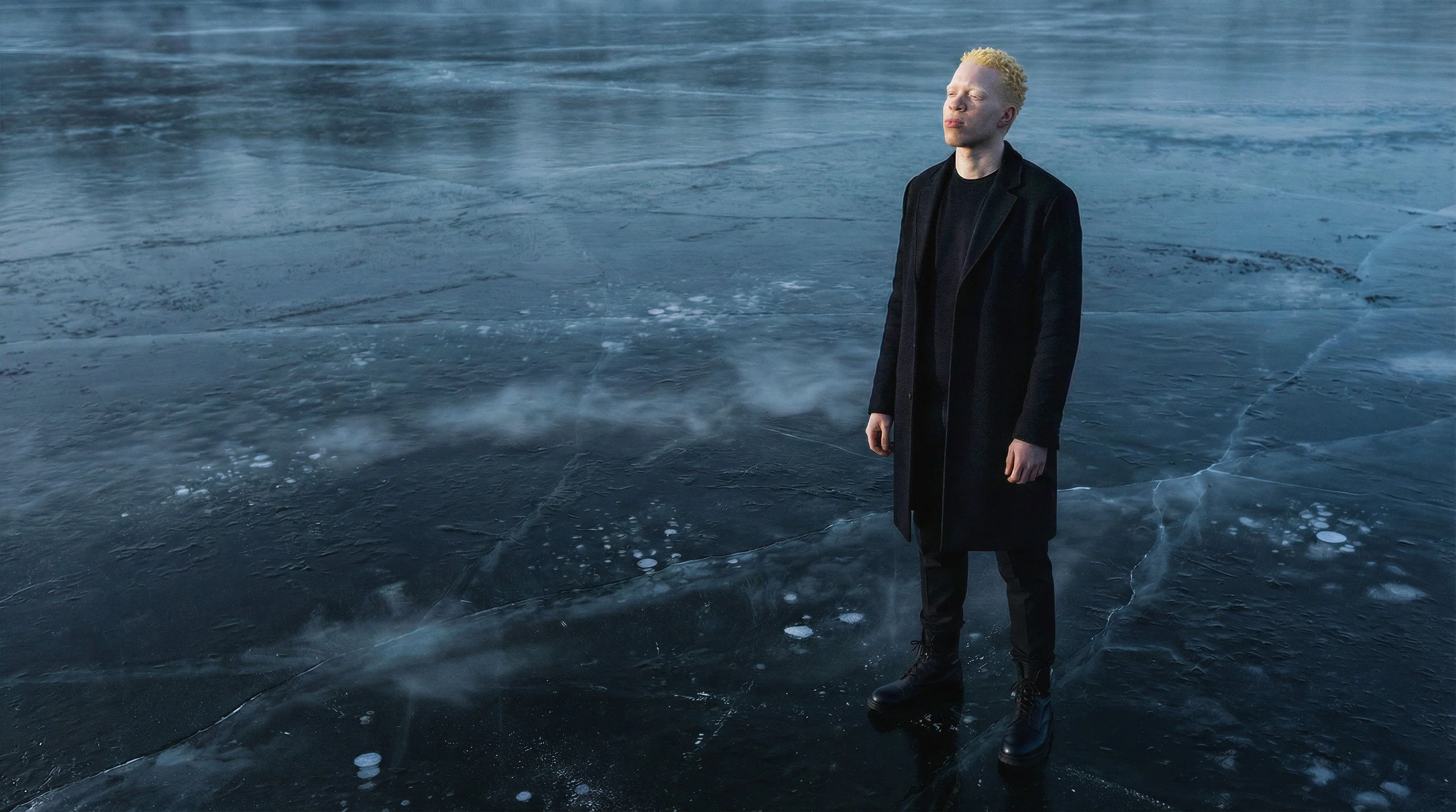 "Full body shot of a digital twin male model wearing a structured black wool coat on a misty, cracked ice field. Synthetic fashion photography for The Arctic Void campaign."