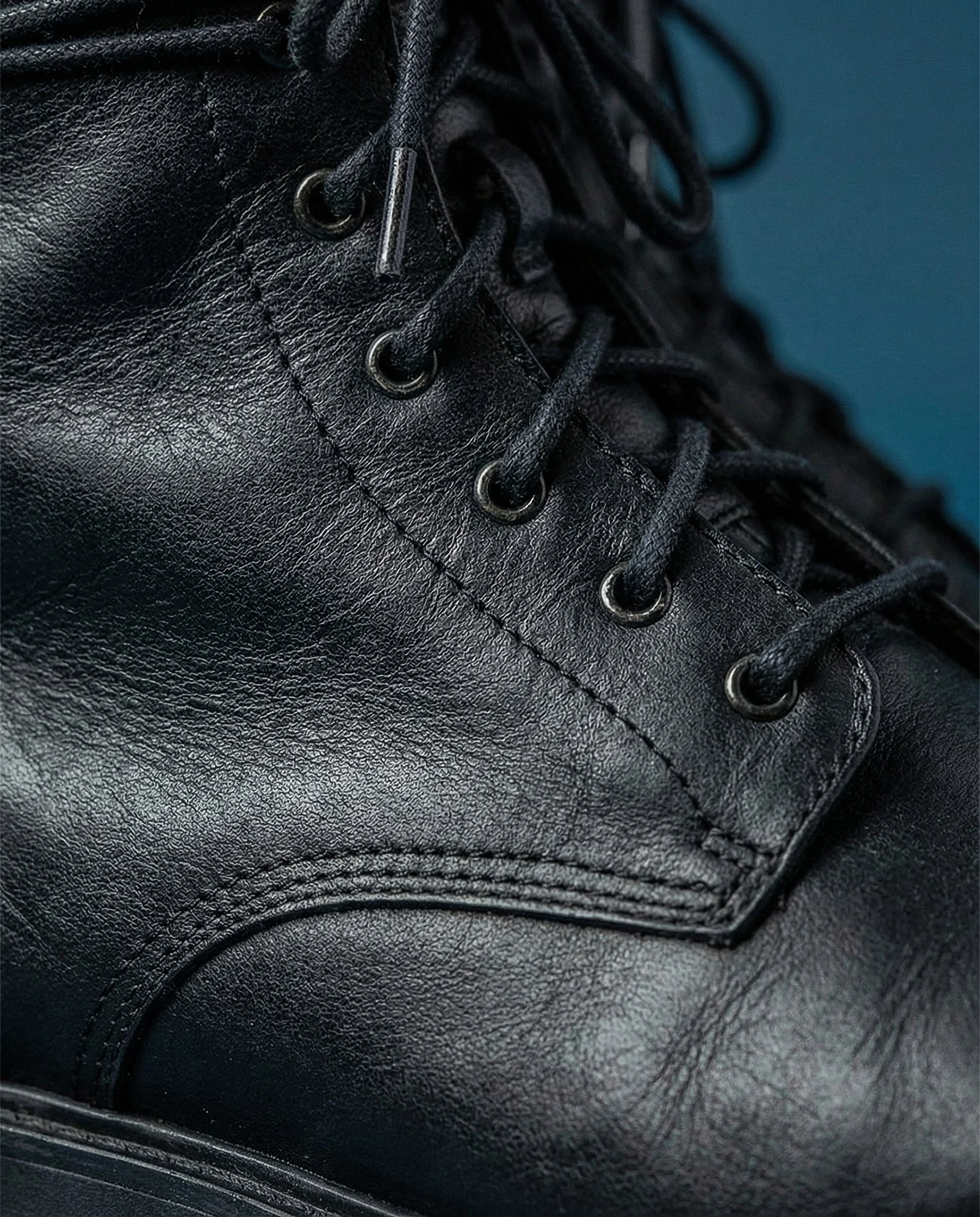 "Extreme close-up of leather grain and laces on a black boot. This macro image highlights the hyper-realistic rendering capabilities of The Raw Lab's AI visual engine."