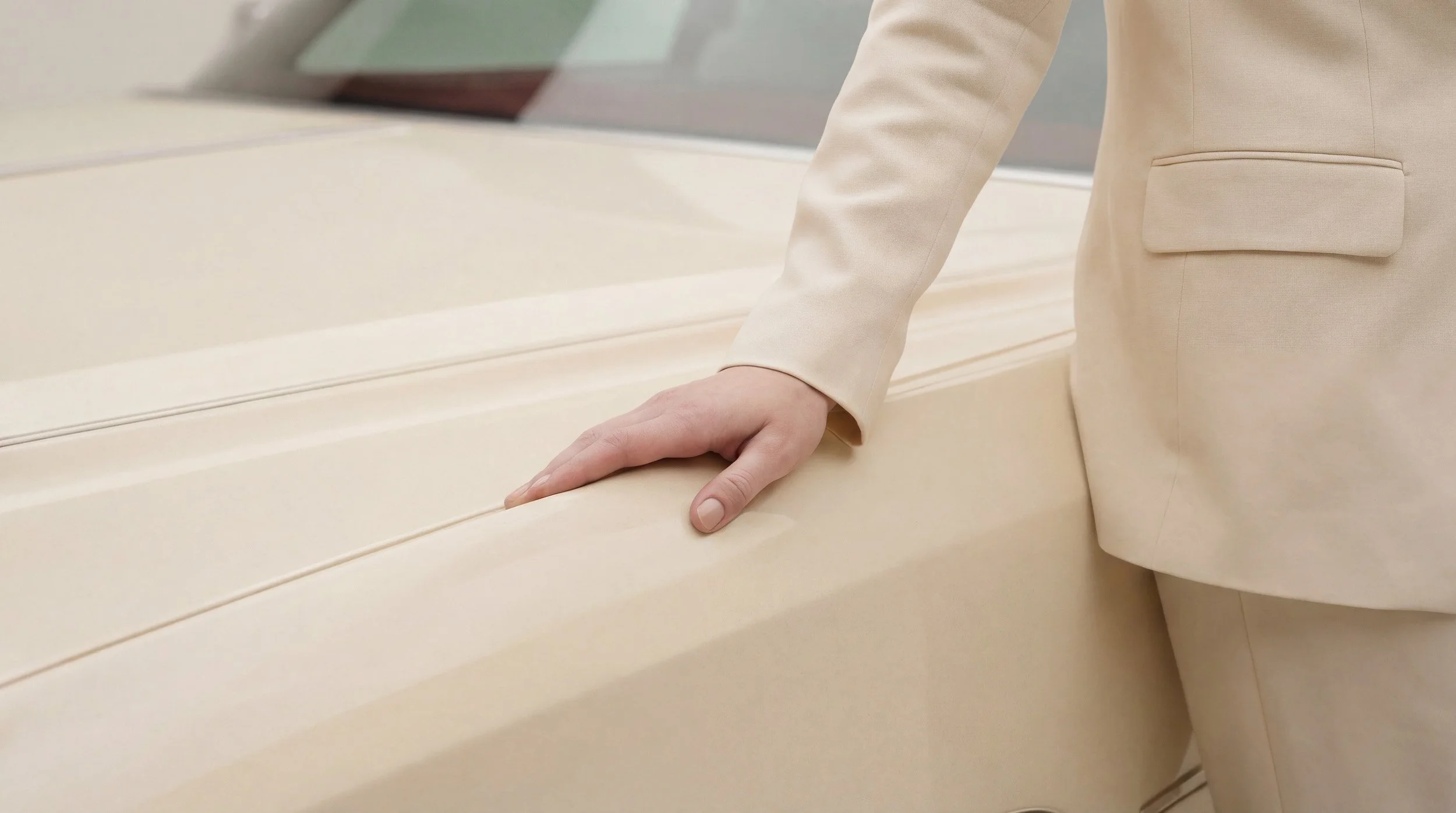 "Close-up of a hand touching the smooth cream surface of a vintage car. Highlighting the precise interaction between human digital twins and synthetic objects."