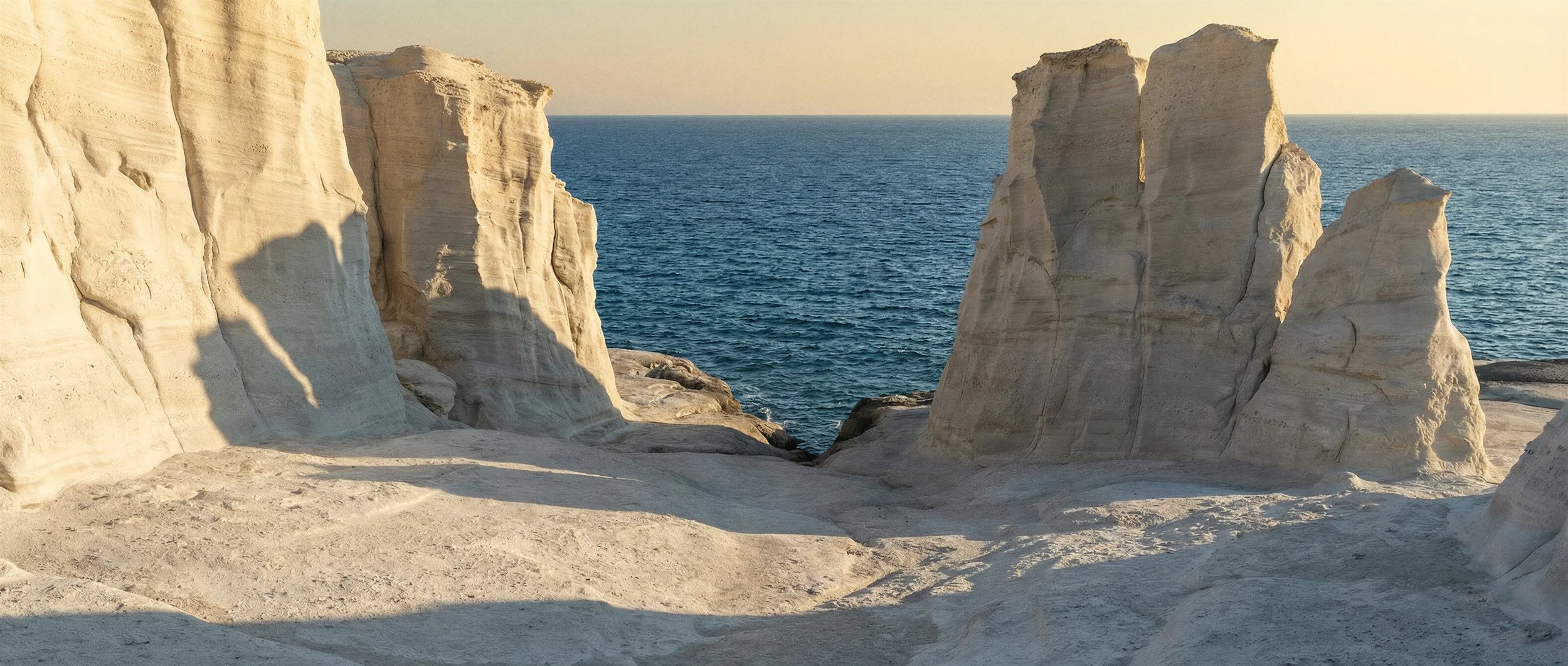 "Wide landscape shot of white limestone cliffs meeting a deep blue Mediterranean sea under golden hour sunlight. A synthetic environment created for high-end fashion campaigns by The Raw Lab's AI engine, eliminating international travel logistics."