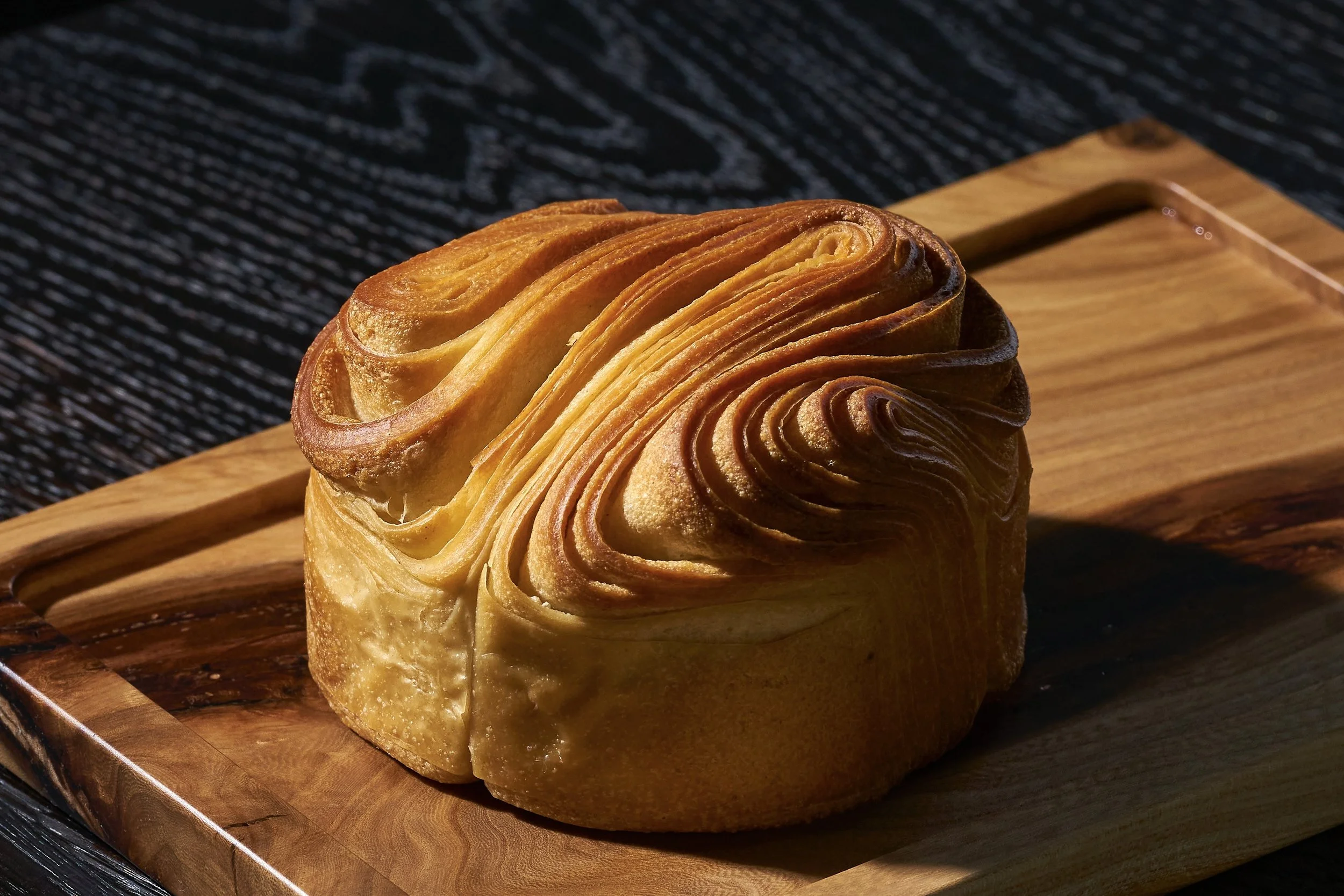 A baked pastry with layered, swirled dough on a wooden serving board.