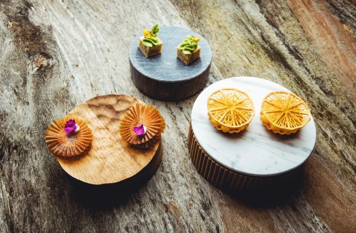 Three decorative desserts on wooden and marble stands with rustic wooden surface by Jaimy Reisinger