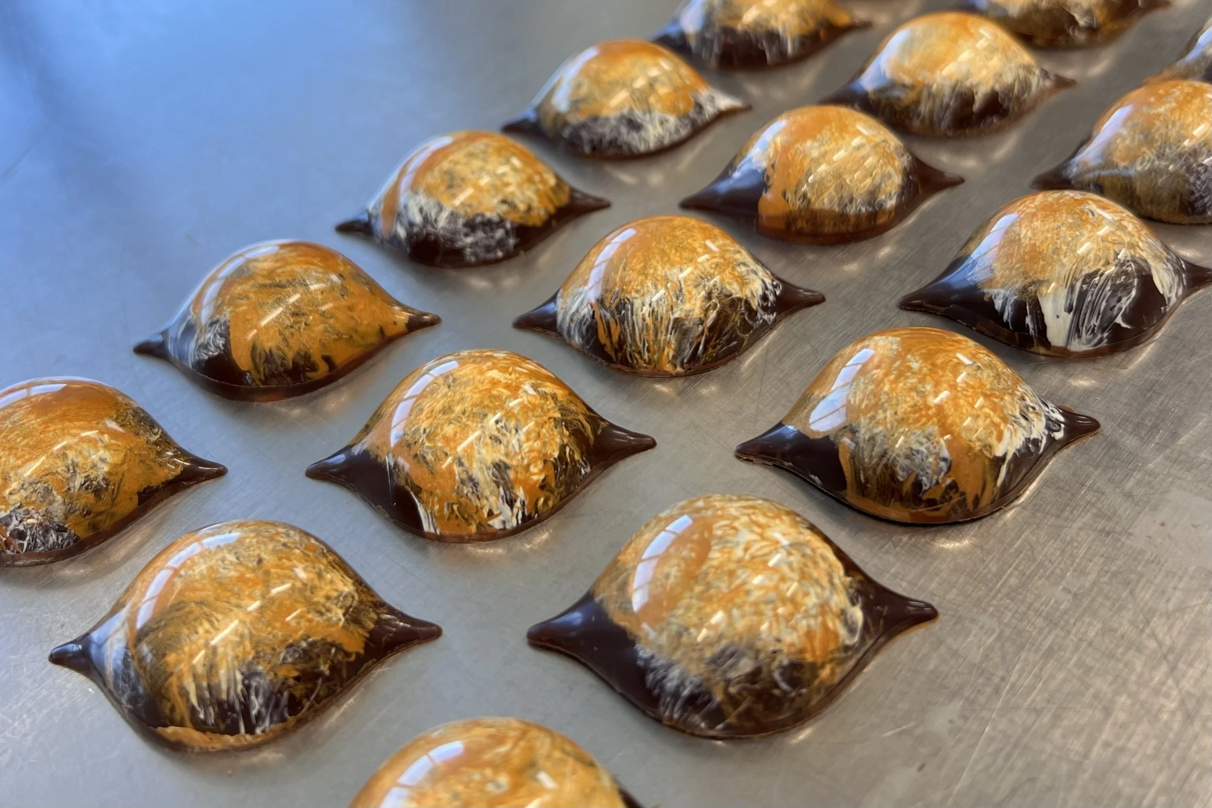 Chocolate candies with caramel and coconut topping on a metal baking sheet.