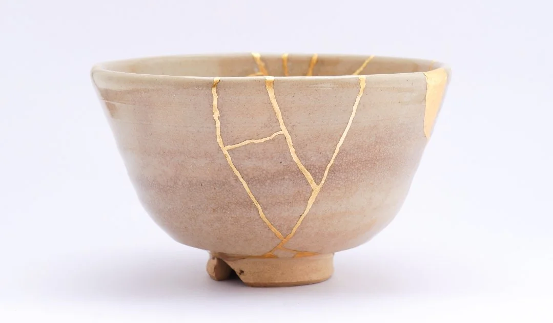 A ceramic bowl with gold lacquer repairs, typical of kintsugi, on a plain white background.