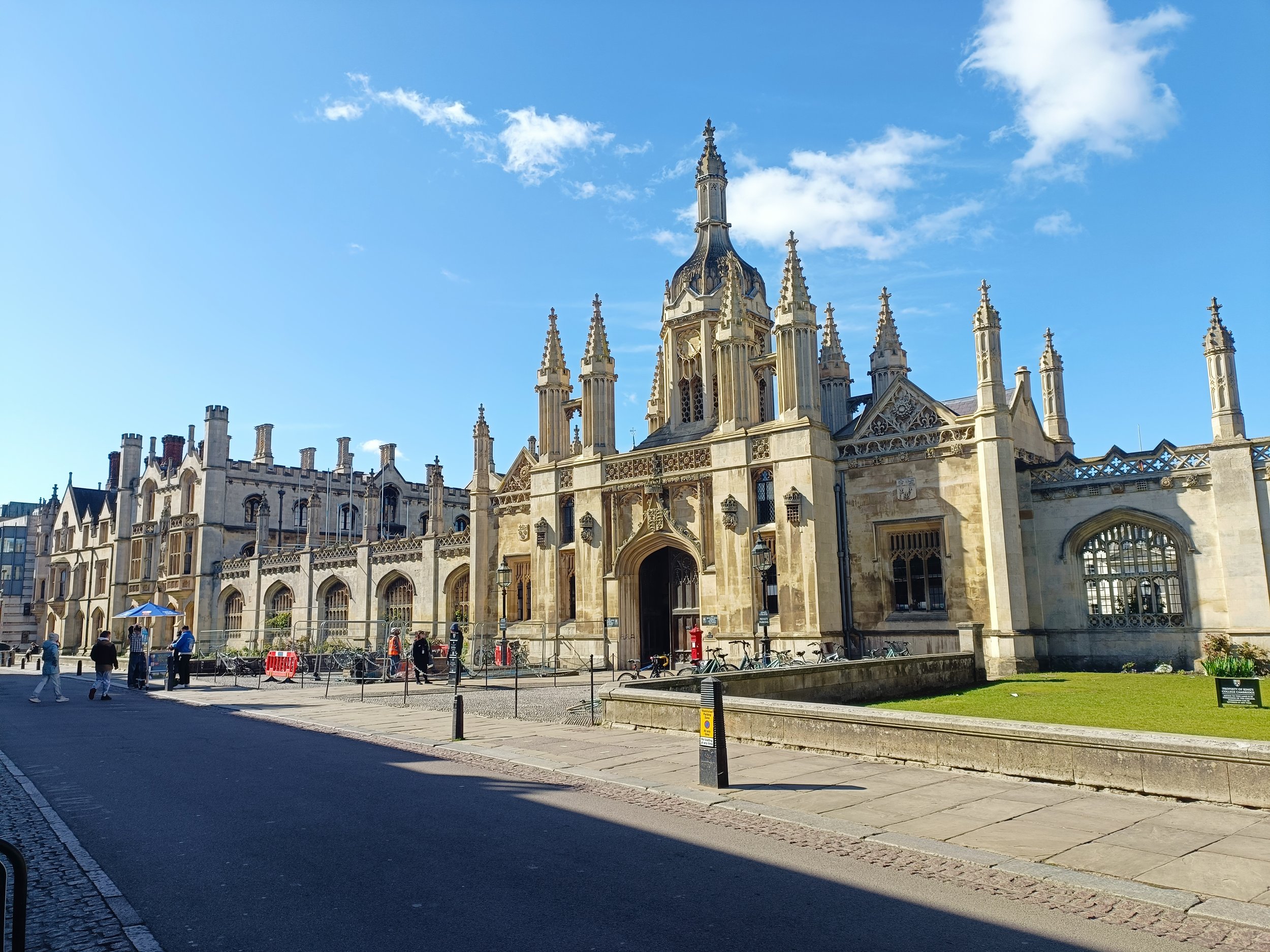 View of a historic Gothic-style building with intricate stonework, pointed arches, and spires, under a bright blue sky with some clouds.