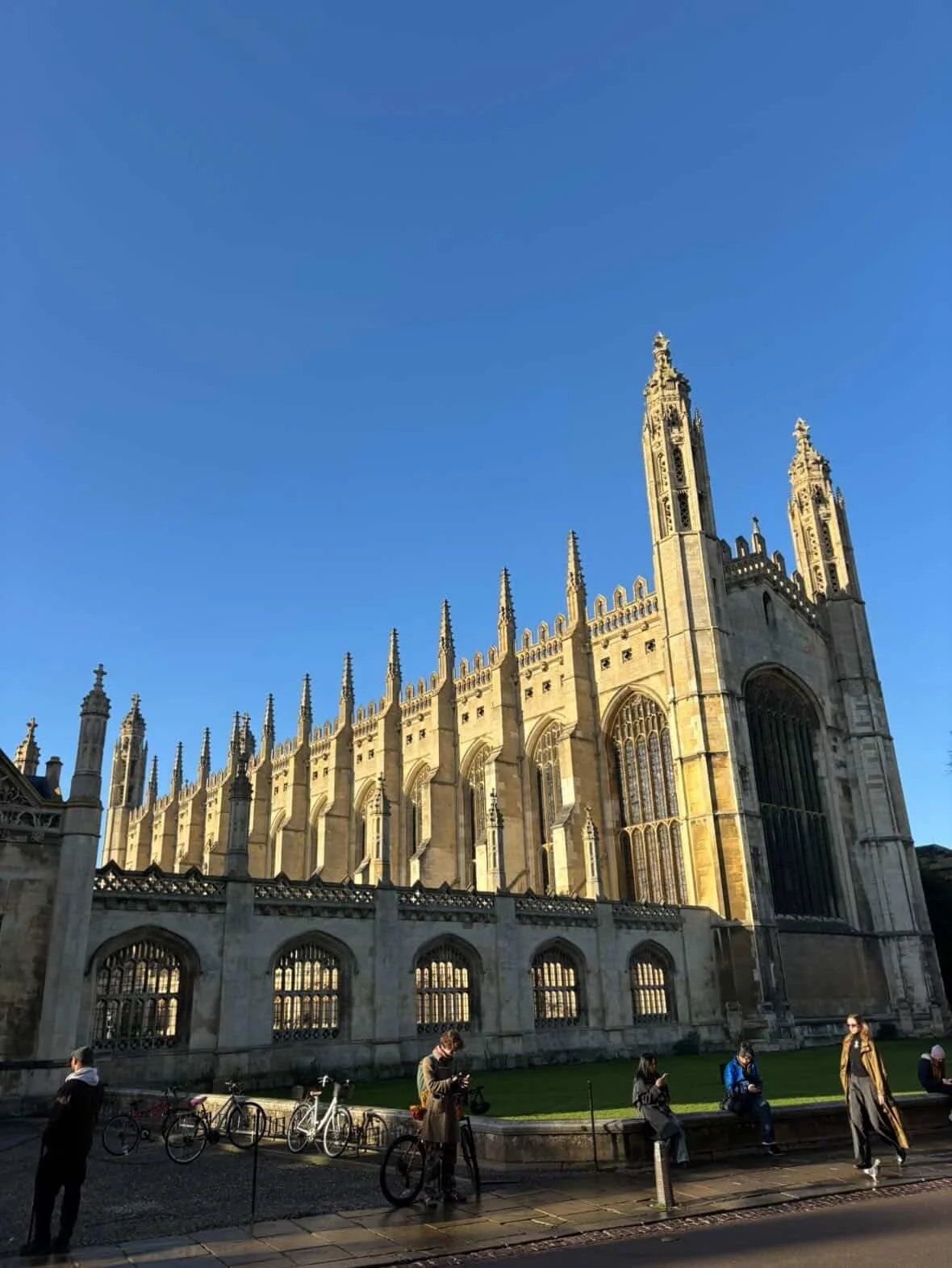 People sitting and standing outside Westminster Abbey under a clear blue sky.