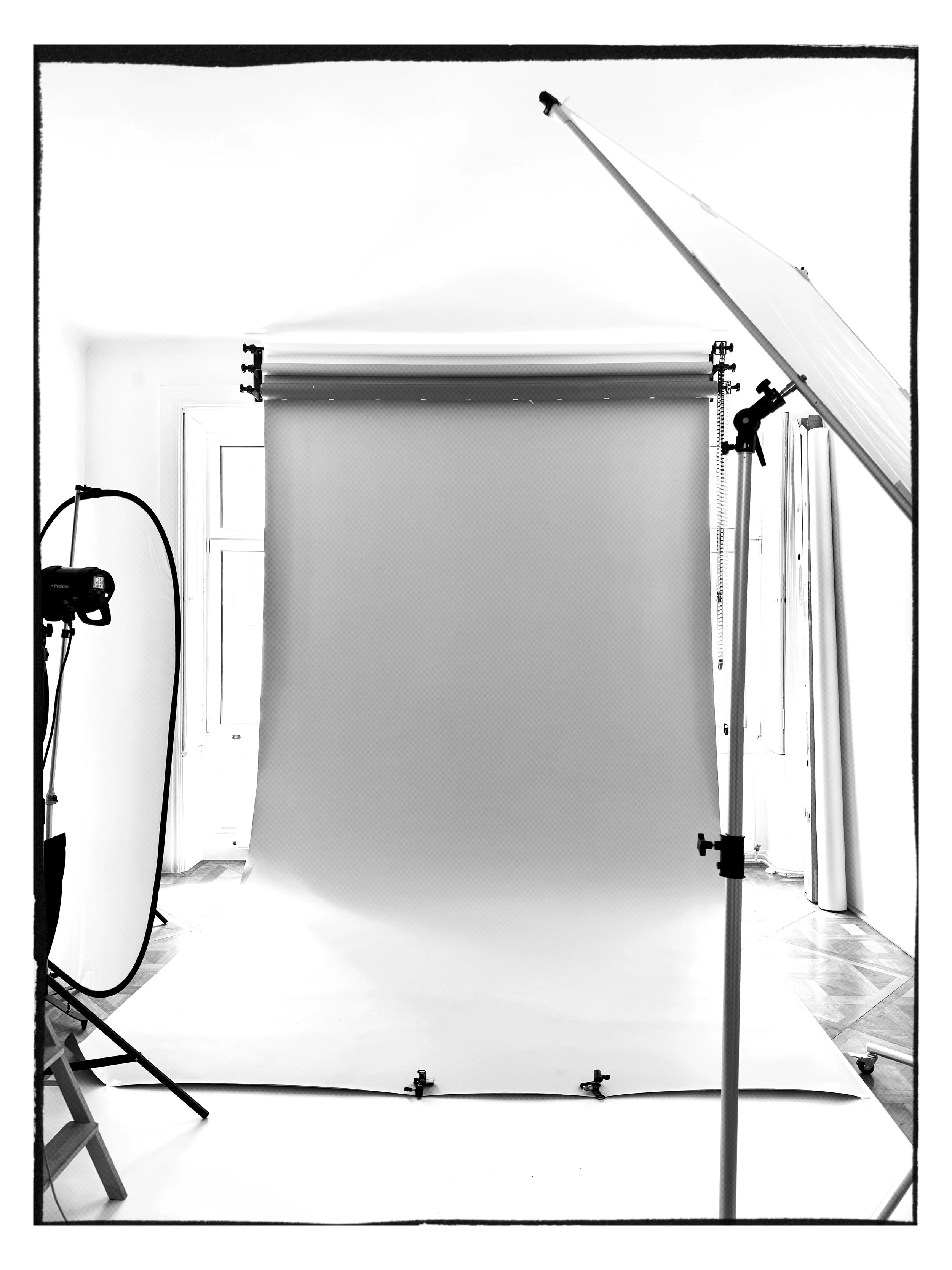 Photography studio setup with a backdrop, studio lights, and equipment in a room with wood floors and a window.