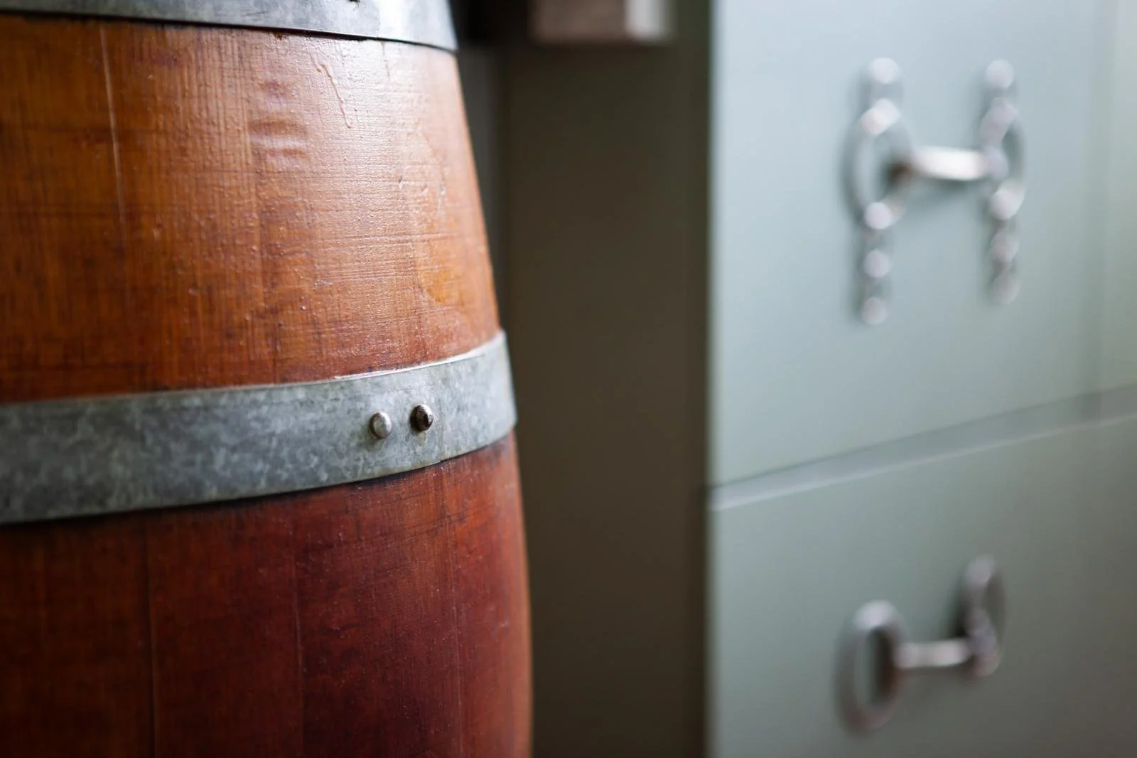 Close-up of a wooden barrel with a metal band, and a light-colored cabinet with metal handles in the background.