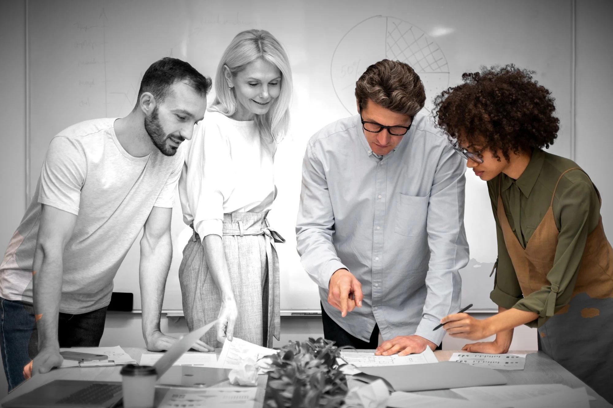 Five diverse professionals collaborate around a table with sketches, papers, and a laptop in a meeting room, discussing a project.